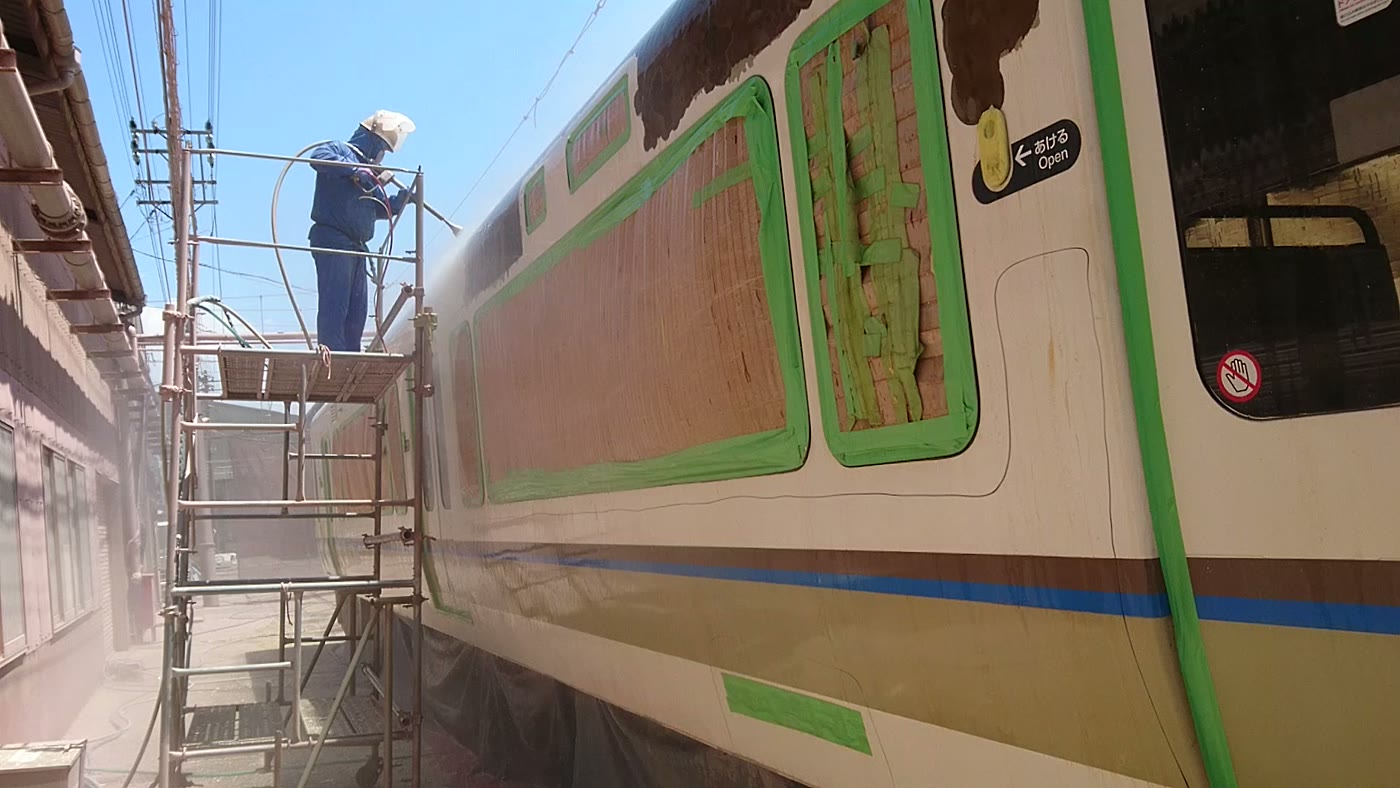 足場の上から鉄道車両の外板塗膜を除去している作業員